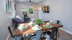 A dining area with a wooden table set for four, surrounded by chairs, a ceiling fan, and a mounted TV.
