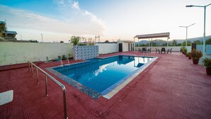 A rooftop swimming pool with a red tiled deck, a covered seating area, and a view of the surrounding landscape. - The Ekling Villa (Udaipur)