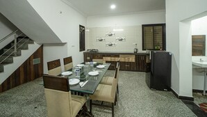 A dining area with a glass table, chairs, and a kitchen in the background. - The Ekling Villa (Udaipur)