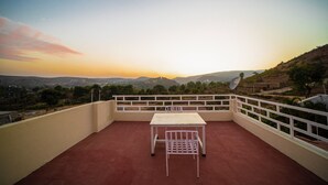 A terrace with a table and chairs, overlooking a scenic landscape with hills and trees. - The Ekling Villa (Udaipur)