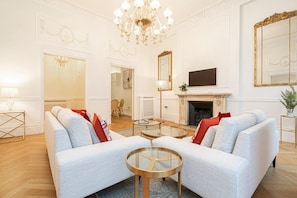 A spacious living room with a white sofa set, a fireplace, a chandelier, and a large mirror. - Beautiful Belgravia (London)
