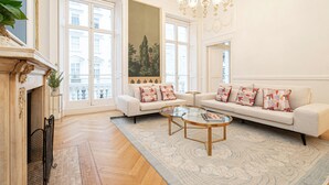 Un salon spacieux doté d’une grande fenêtre, d’une cheminée, d’un lustre et d’un ensemble de canapés.