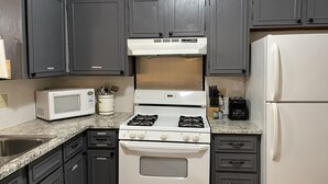 A kitchen with dark cabinets, a white stove, a microwave, and a refrigerator. - TXST Cozy and centrally located (San Marcos)