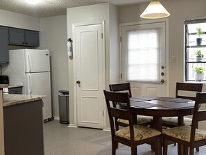 A compact kitchen with a refrigerator, a trash can, and a window with blinds. - TXST Cozy and centrally located (San Marcos)