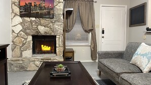 A living room with a stone fireplace, a mounted TV, a sofa, and a coffee table with a decorative item. - TXST Cozy and centrally located (San Marcos)