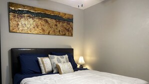 A bedroom with a large bed, a headboard, and a nightstand with a lamp. - TXST Cozy and centrally located (San Marcos)