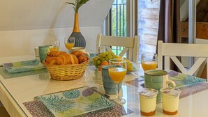 Et morgenbord med croissanter, frugt og juice, placeret i et rum med træpaneler og udsigt gennem et vindue.