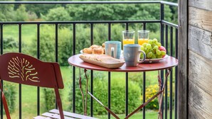 En balkon med et bord dækket til morgenmad, inklusive croissanter, frugt og glas med juice.