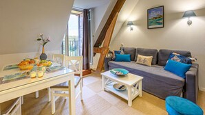 Hyggelig loftrum med opholdstue, spiseområde, en grå sofa med farverige puder og udsigt til det fri.