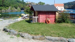 Une petite construction en bois rouge, dotée d’un toit incliné, d’une balançoire et d’une jetée qui s’avance sur un lac paisible.