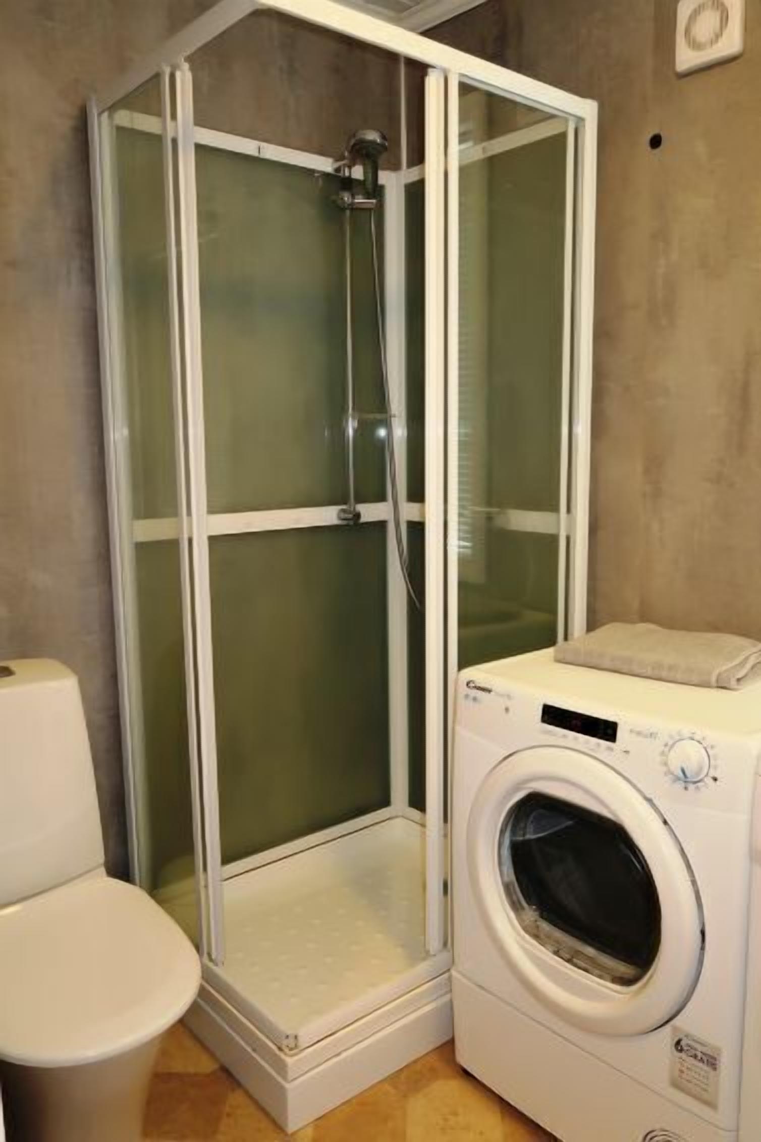 A bathroom with a glass-enclosed shower, a toilet, and a front-loading washing machine.