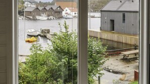 Une vue depuis une fenêtre donnant sur un quai avec des bateaux, une jetée en bois et des bâtiments en arrière-plan.