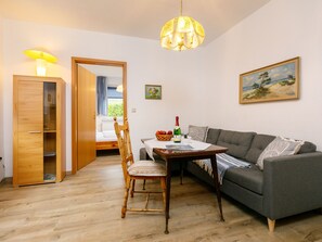 Un salon chaleureux avec une armoire en bois, une table à manger avec une chaise, un canapé gris et un tableau accroché au mur.