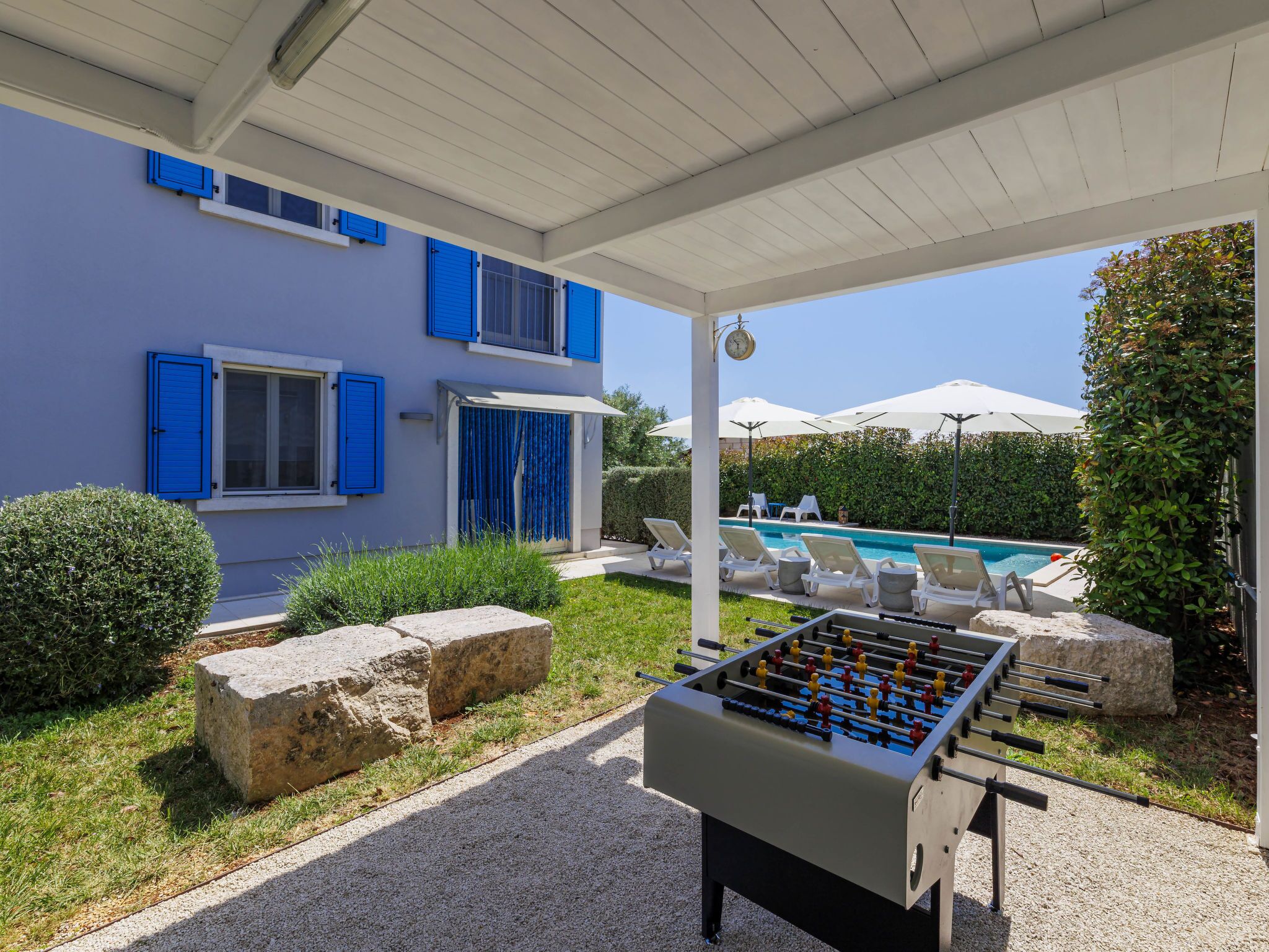 A pool area with lounge chairs, a foosball table, and a covered patio with a clock.