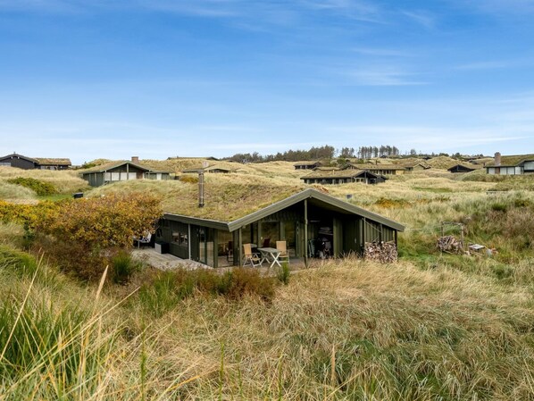 Un edificio moderno y ecológico con techo inclinado, rodeado de un paisaje cubierto de césped y otras estructuras similares.
