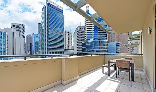 Un balcon offrant une vue sur des immeubles modernes, une table avec des chaises et un petit coin salon.