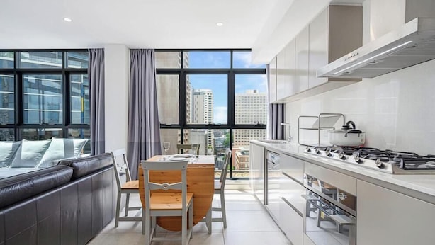 A modern kitchen with a dining area, large windows, and a view of the city. - MetaWiseBnB|Sydney CBD|Chinatown|Luxe 2Bed Penthouse Bella (Haymarket)