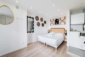 A bedroom with a bed, bedside table, lamp, and a washing machine in the corner.