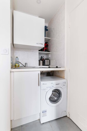 A compact laundry area with a washing machine, a sink, and a cabinet above the counter.