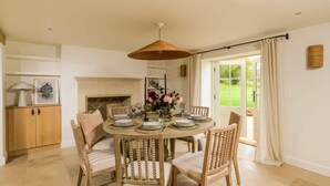 A dining room with a round table set for six, surrounded by wooden chairs with cushioned seats. A woven pendant light hangs above the table, and a vase with flowers is placed in the center. - Beautiful Farmhouse & Garden in Heart of Somerset (Yeovil)