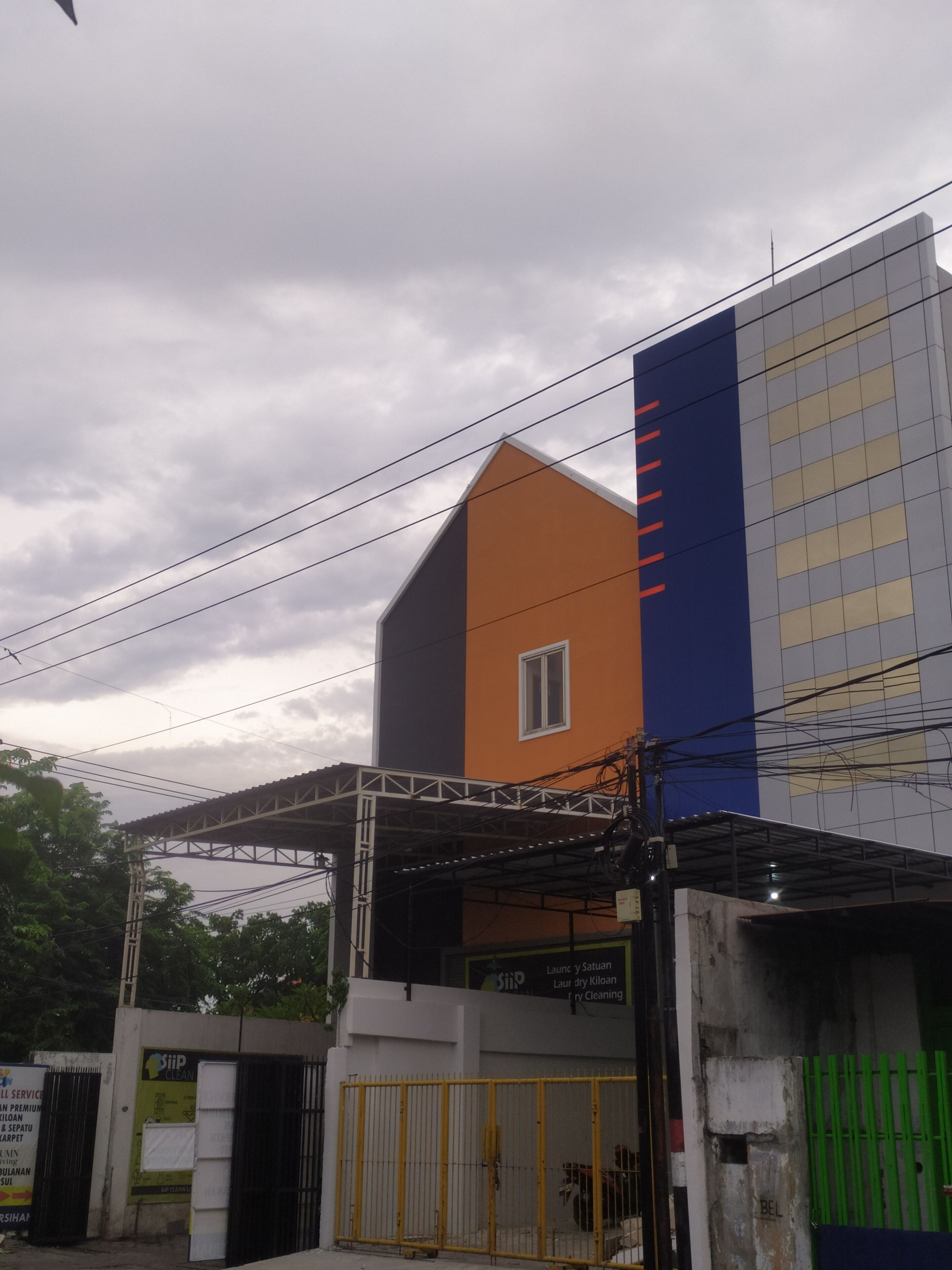 A multi-story building with a prominent orange and blue facade, a gated entrance, and visible signage for a cleaning service.