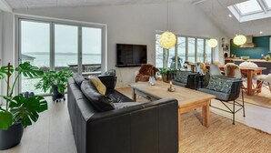 A spacious living room with a large black leather sofa, a wooden dining table, and a view of the sea through large windows. - "Lika" - 25m to the fjord by Interhome (Nordborg)
