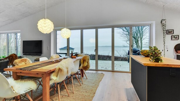 A modern dining area with a wooden table, white chairs, and a large window overlooking a body of water. - "Lika" - 25m to the fjord by Interhome (Nordborg)