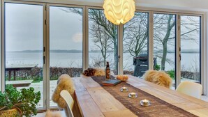 A dining area with a wooden table, candles, and a view of a lake through large glass doors. - "Lika" - 25m to the fjord by Interhome (Nordborg)