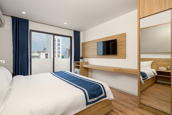 A modern hotel room with a large bed, a TV mounted on the wall, and a sliding door leading to a balcony.