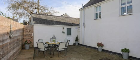 Une cour avec une table et des chaises, un bâtiment blanc et une clôture en bois.