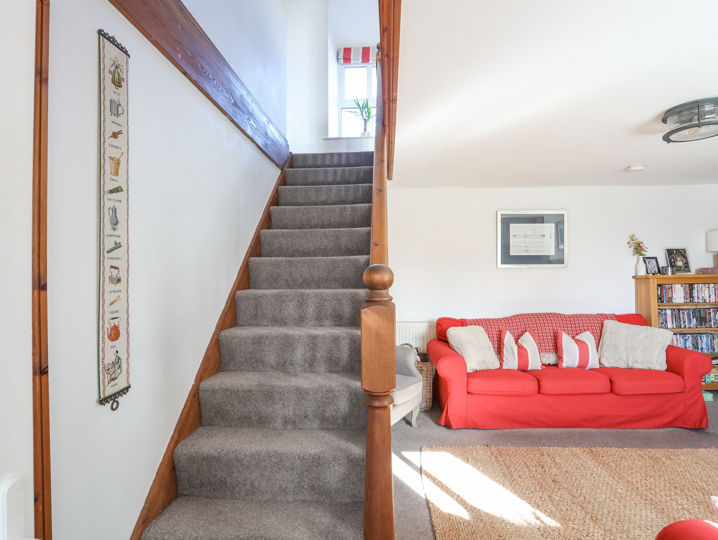 Eine Holztreppe mit Geländer führt in ein Wohnzimmer mit einem roten Sofa und einem Bücherregal.