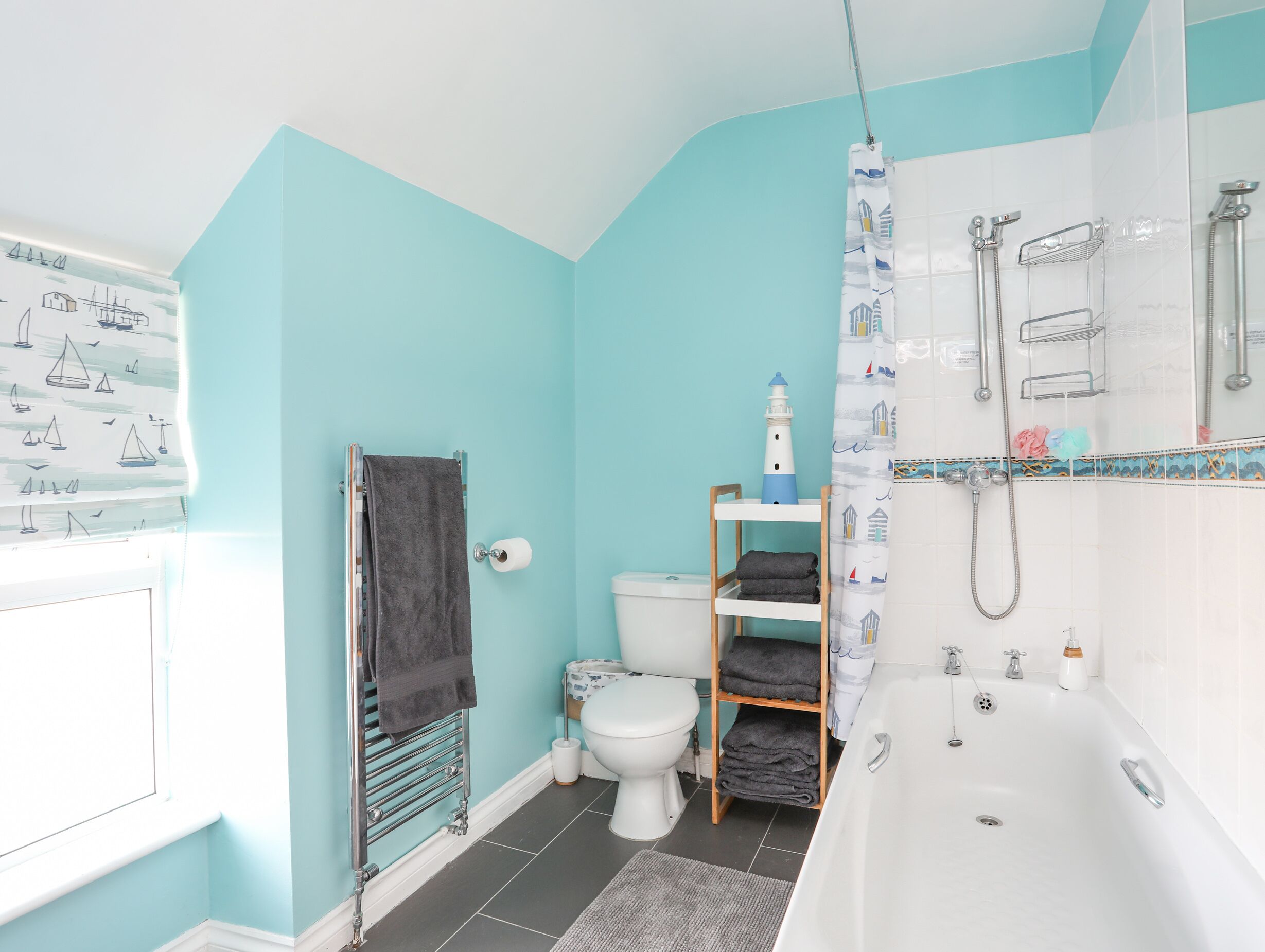 A modern bathroom with a blue wall, a white bathtub, a shower, and a toilet.