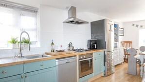 A modern kitchen with a stainless steel range hood, a built-in dishwasher, and a coffee maker on the countertop. - Bron Gadair (Pwllheli)