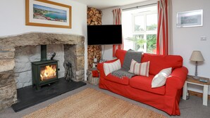 A cozy living room with a stone fireplace, a red sofa, and a television on the wall. - Bron Gadair (Pwllheli)