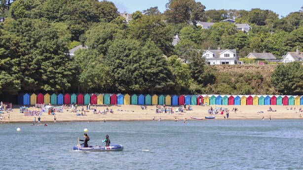 A beach with colorful beach huts and a row of houses in the background. - Bron Gadair (Pwllheli)