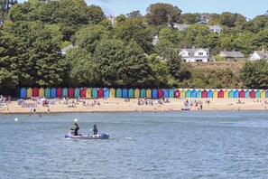 A beach with colorful beach huts and a row of houses in the background. - Bron Gadair (Pwllheli)