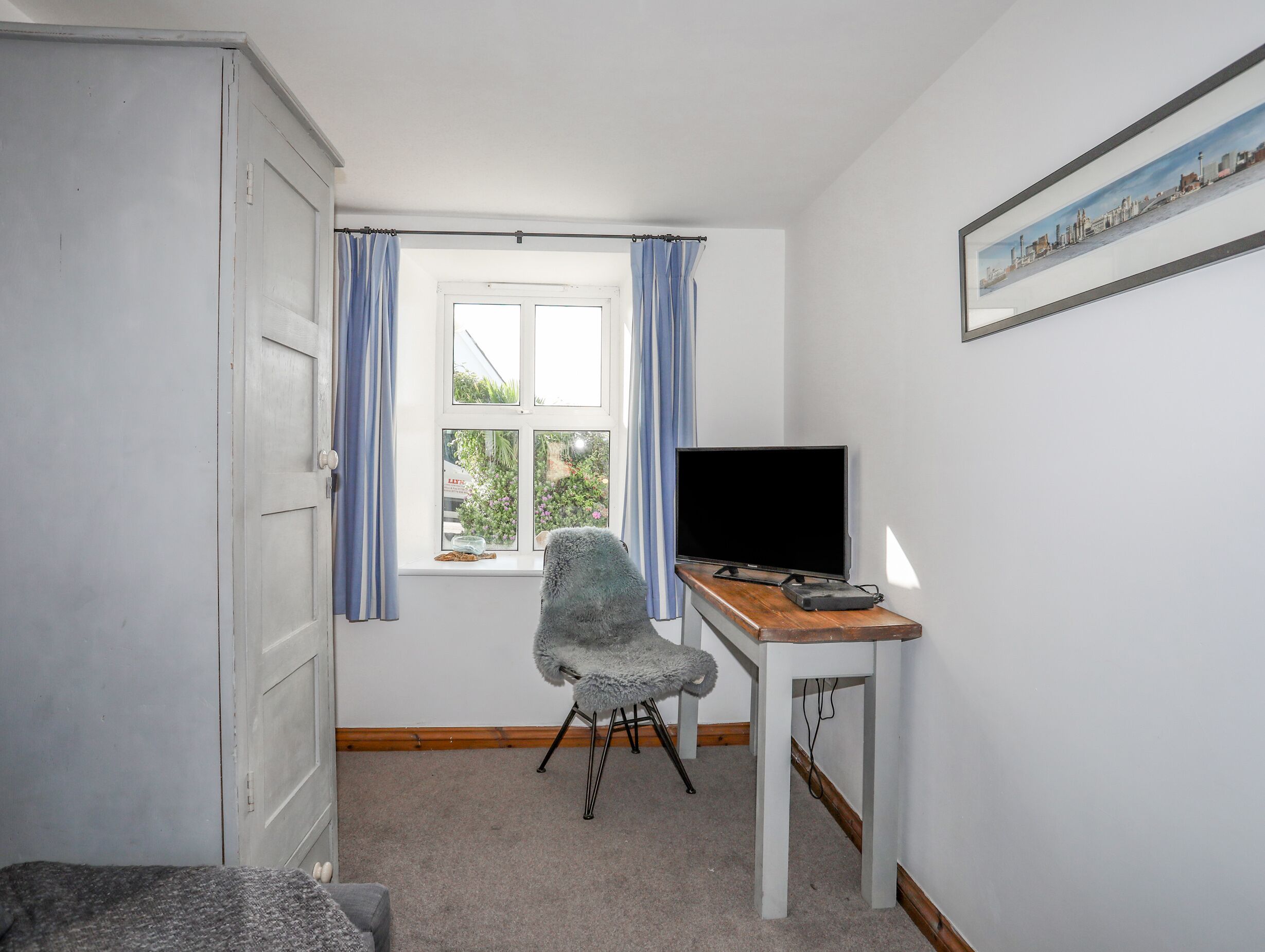 A small, sparsely furnished room with a desk, chair, and a television.