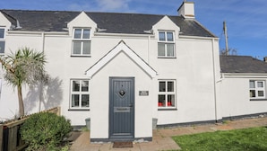 A white two-story house with a dark blue door, a small porch, and a sign reading "BRON GADAIR". - Bron Gadair (Pwllheli)