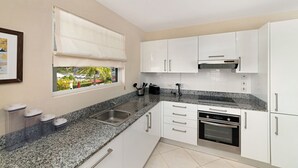 Una cuina moderna amb armaris blancs, encimeres de granat i un rentaplat amb acabat d'acer inoxidable, i forn.