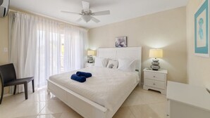 Habitació d'hotel amb un llit, dues taules de nit amb làmpades, una cadira, un ventilador de sostre i una finestra amb cortines.