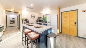 A modern kitchen with a central island, bar stools, a refrigerator, and a clock on the wall. - Starry Night Cabin at Sky Ranch (Oakhurst)