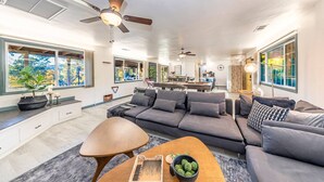 A spacious living room with a large gray sofa, a wooden coffee table, and a dining area in the background. - Starry Night Cabin at Sky Ranch (Oakhurst)