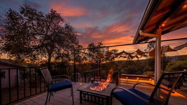 An outdoor deck with a fire feature, seating, and a view of trees and a sunset. - Starry Night Cabin at Sky Ranch (Oakhurst)