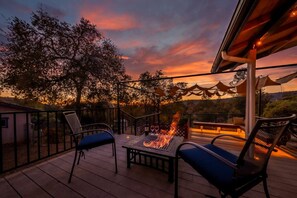 An outdoor deck with a fire feature, seating, and a view of trees and a sunset. - Starry Night Cabin at Sky Ranch (Oakhurst)