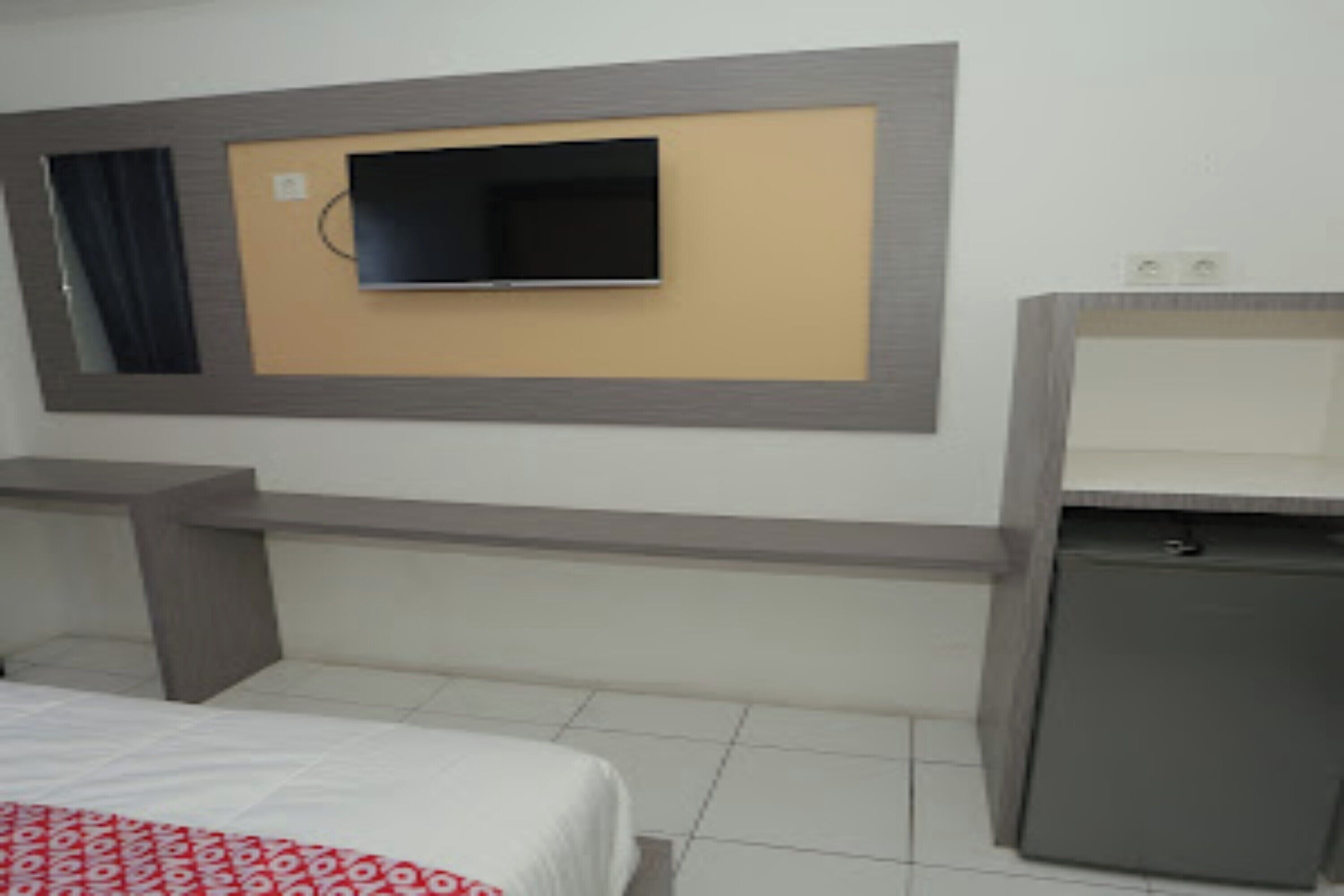Habitación de hotel con cama, televisión montada en la pared, escritorio pequeño y un refrigerador miniatura.
