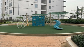 A playground with climbing structures and a slide, surrounded by a landscaped area with a building in the background. - OYO Life 92859 Biant House (Cikarang)