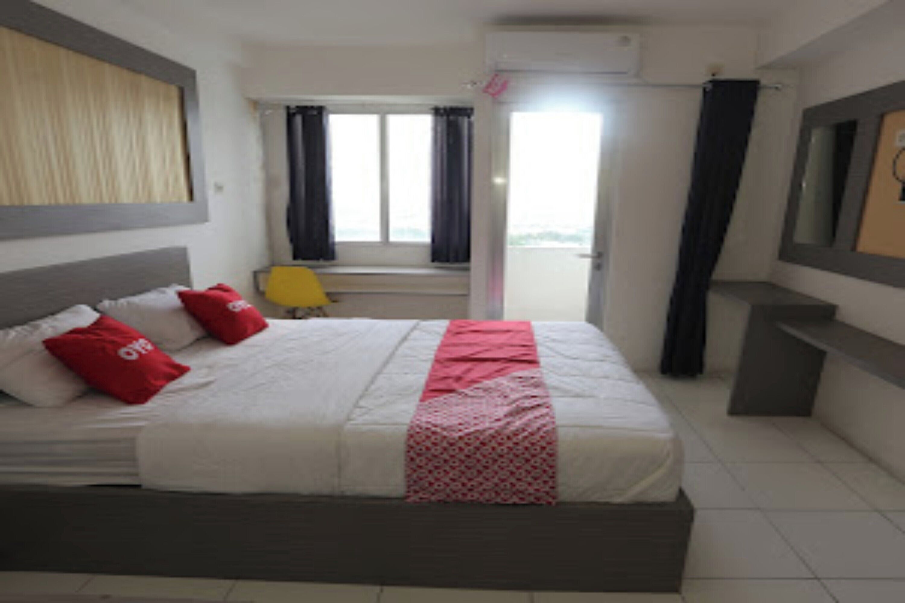 Une chambre d’hôtel avec un lit, une fenêtre avec des rideaux, une petite table et un miroir au mur.