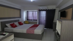 A hotel room with a bed, a desk, a chair, a TV, and a window with curtains. - OYO Life 92859 Biant House (Cikarang)