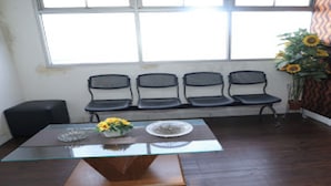 A room with a glass-top table, a black bench along the wall, and a window with curtains. - OYO Life 92859 Biant House (Cikarang)