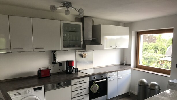 A modern kitchen with white cabinets, a Bosch washing machine, a coffee maker, and a window with a view of greenery. - Large apartment with 2 bathrooms and 2 large parking spaces (Leichlingen (Rheinland))
